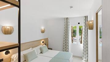 Habitación de hotel con cama, lámparas de noche, ventana con cortinas y vistas al exterior.