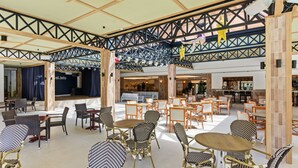 Amplio espacio interior con varios arreglos de asientos, incluyendo mesas y sillas, y una zona de escenario al fondo.