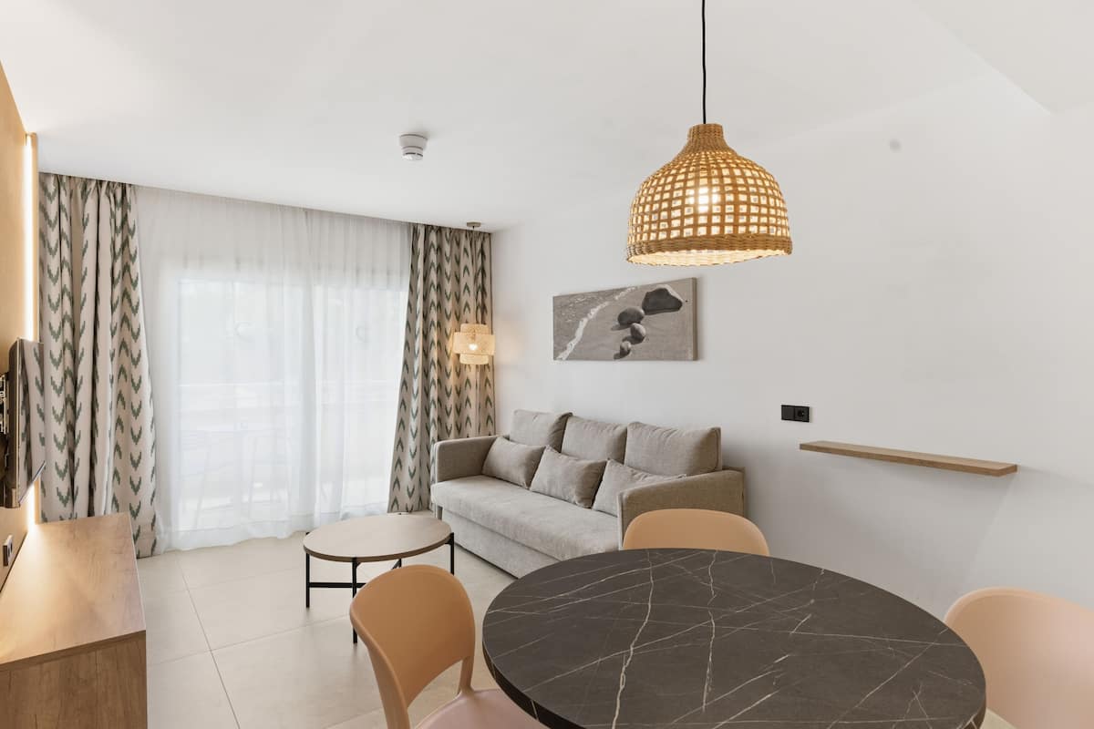 A modern living room with a sofa, a dining table, and a hanging light fixture.