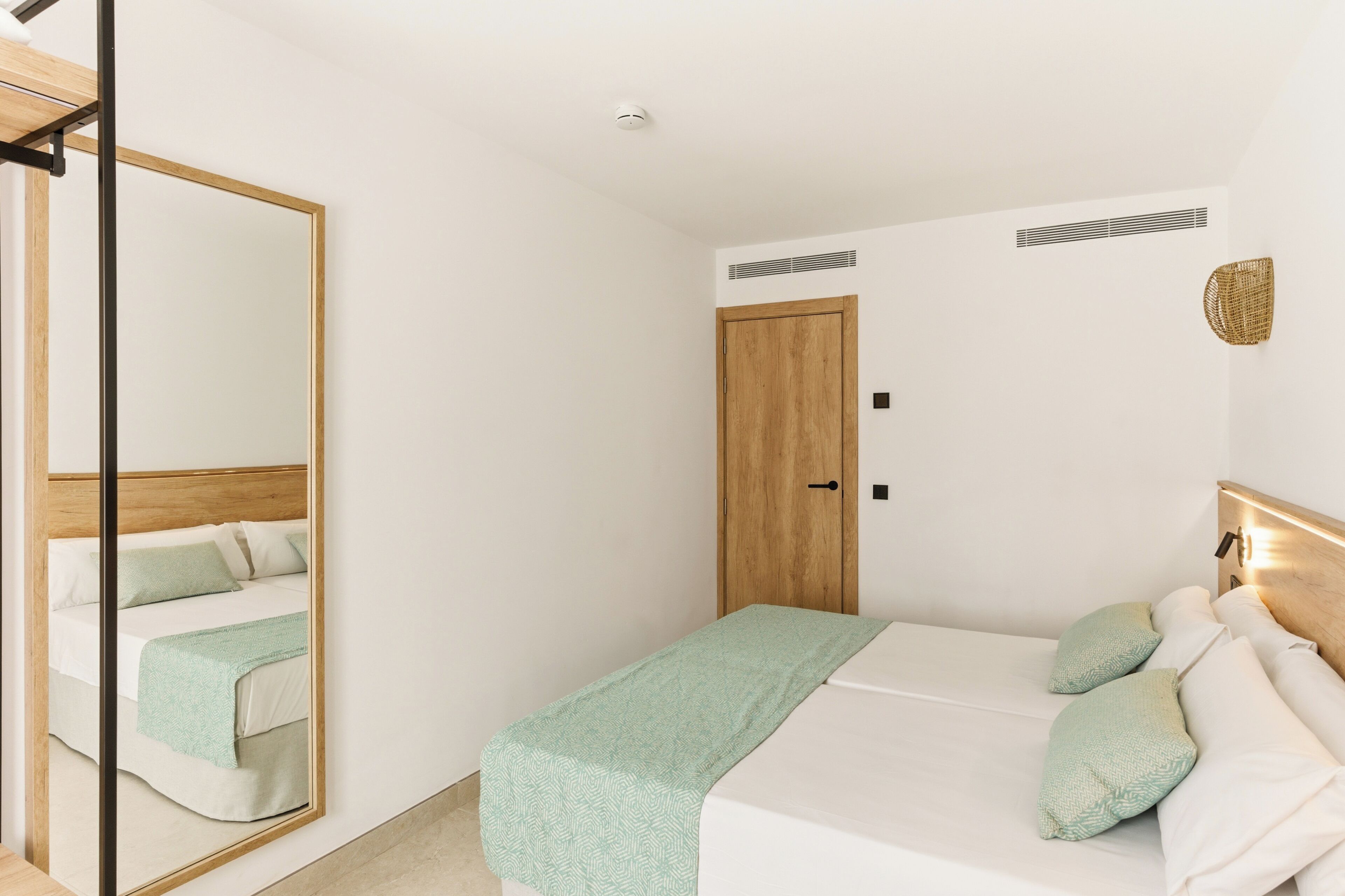 Une chambre à coucher avec un lit, une porte en bois, un miroir et un luminaire fixé au mur.
