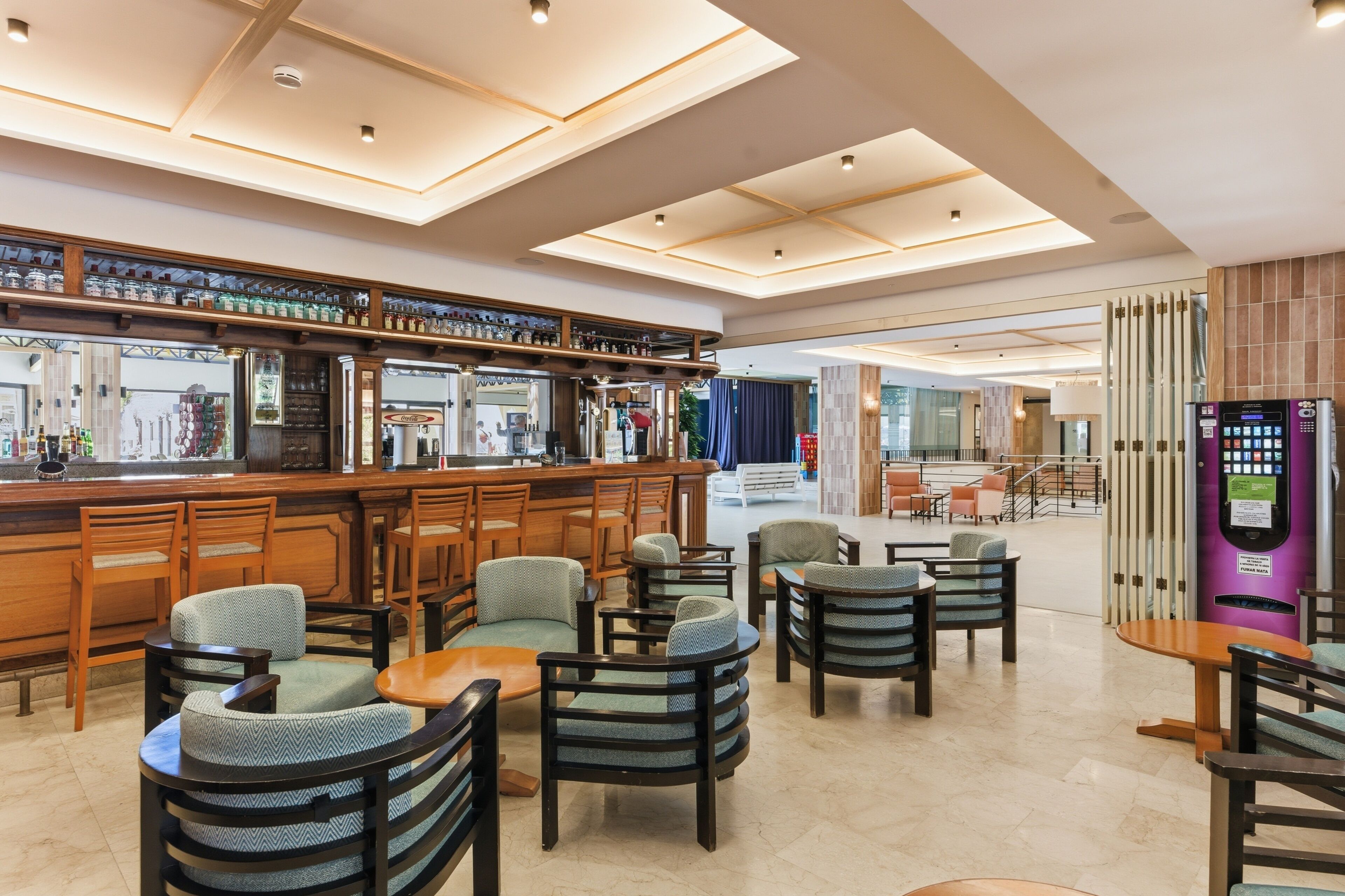 A modern bar area with seating, a vending machine, and a view of the lobby.