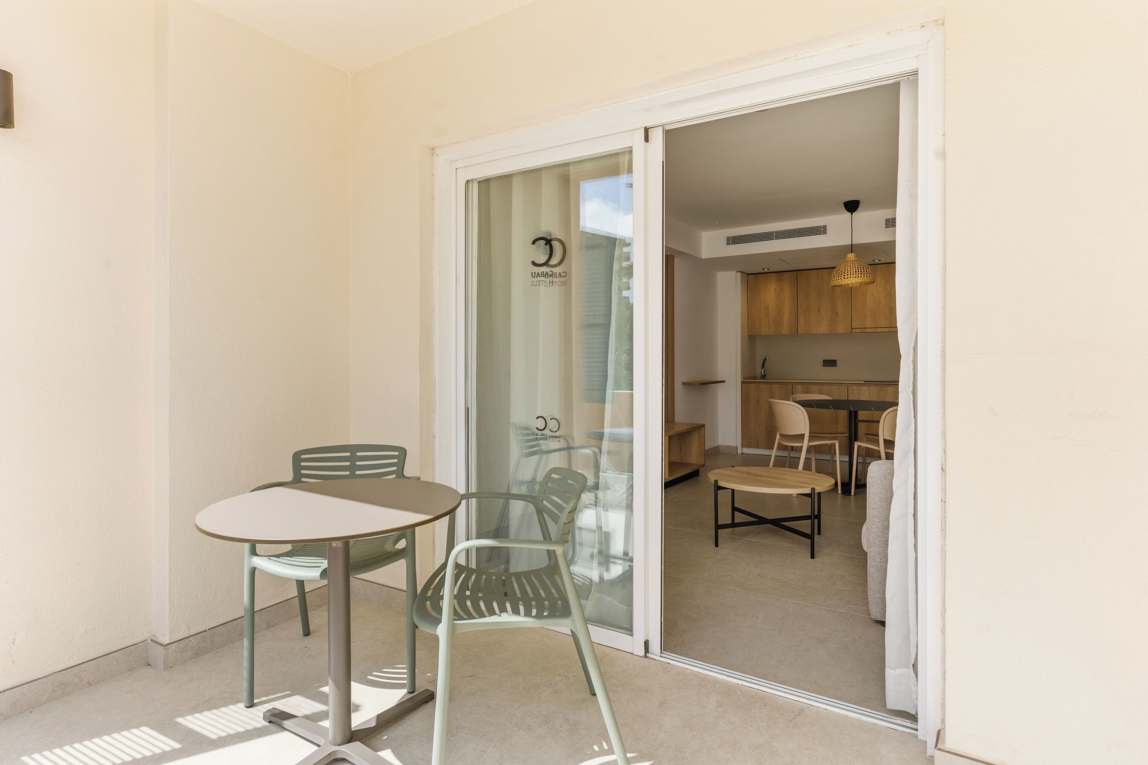 A small dining area with a table and chairs, a glass door leading to a kitchen, and a ceiling light fixture.