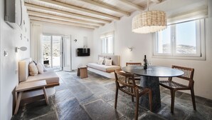 Een modern interieur met een stenen vloer, houten balken in het plafond, een ronde eettafel met stoelen, een bank en een aan de muur bevestigde televisie.