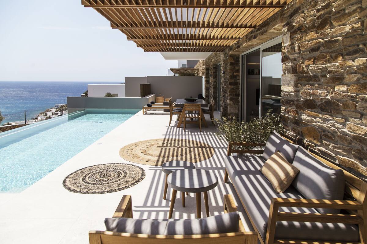 Un espace aménagé au bord de la piscine, avec vue sur la mer, doté de mobilier en bois et de murs en pierre.
