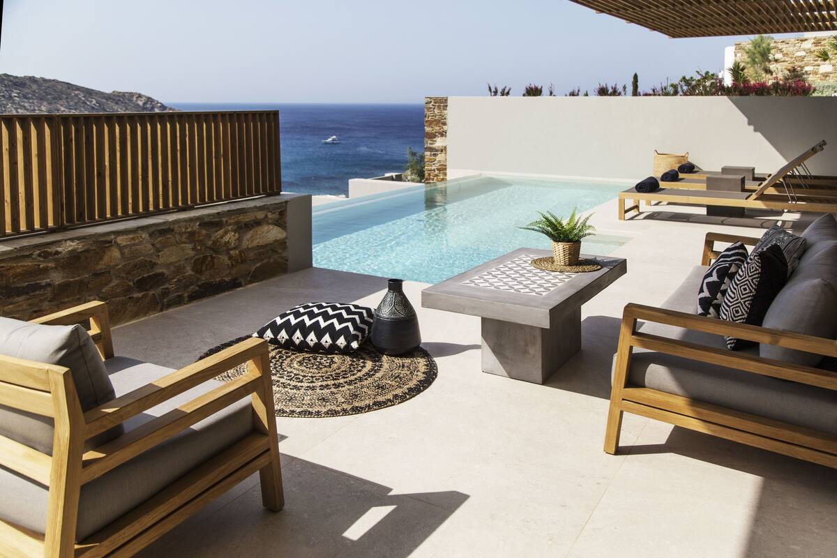Un espace extérieur moderne, aménagé avec des sièges, une piscine, des murs en pierre et une vue sur la mer.
