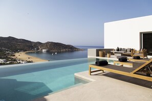 A modern pool area with a view of a beach and mountains. - Hide out Suites (Ios)