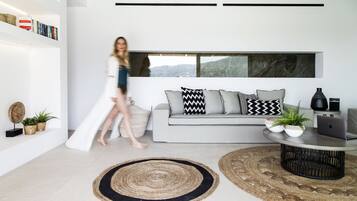 A modern living room with a grey sofa, black and white patterned pillows, a round coffee table, and two potted plants.