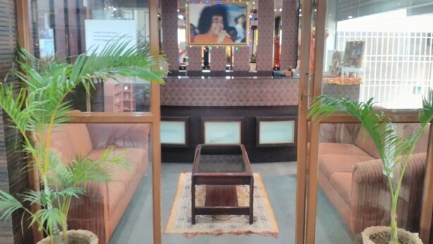 A reception area with a sofa, a coffee table, and two potted plants. - Sai Pavilion (Puttaparti)