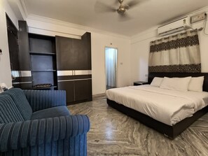 A bedroom with a bed, a sofa, a wardrobe, and a ceiling fan. - Sai Pavilion (Puttaparti)