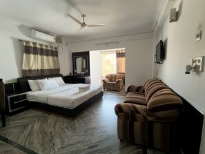 A hotel room with a bed, a sofa, a television, and an air conditioning unit. - Sai Pavilion (Puttaparti)