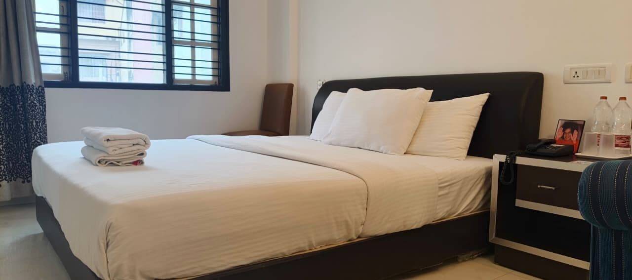 Una camera d'albergo con un letto, un comodino, una sedia e una finestra con persiane.