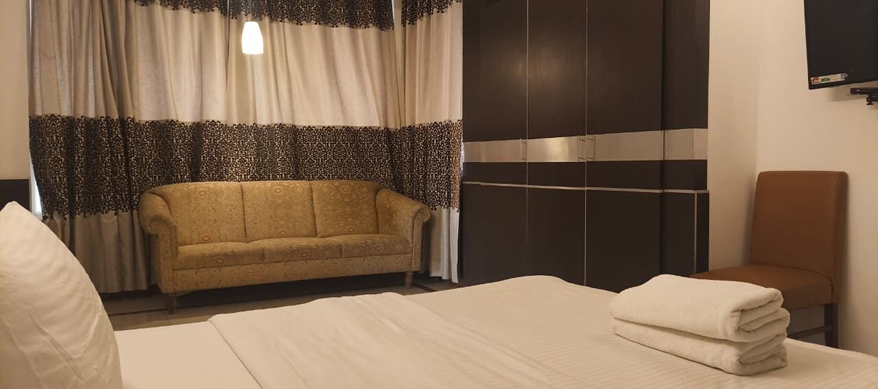 A hotel room with a bed, a sofa, a chair, and curtains.