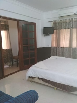 A bedroom with a bed, a television mounted on the wall, and a sliding glass door leading to another room.