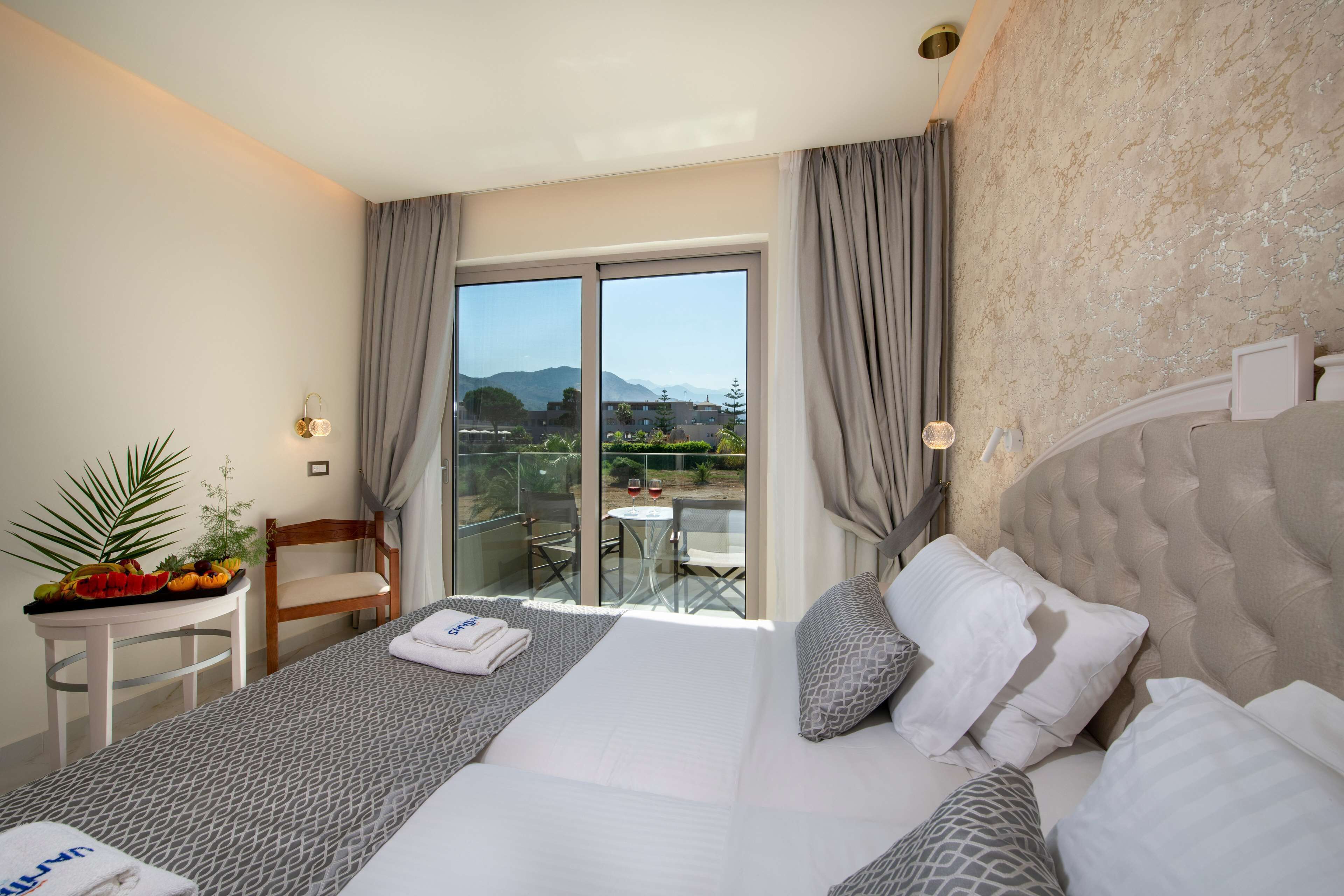 Ein Hotelzimmer mit einem großen Bett, einem kleinen Tisch mit einer Pflanze und Blick ins Freie.