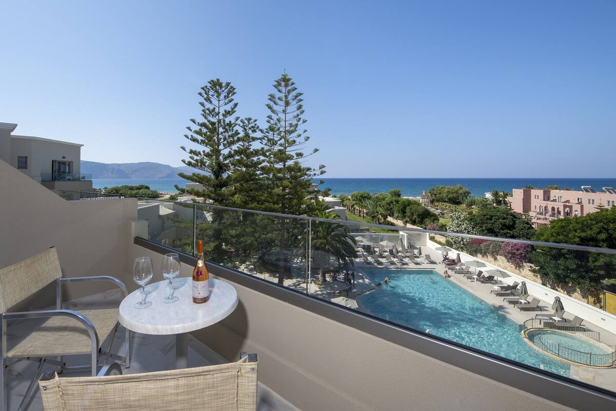 Uma varanda com piscina, cadeiras e uma mesa com copos de vinho e uma garrafa.