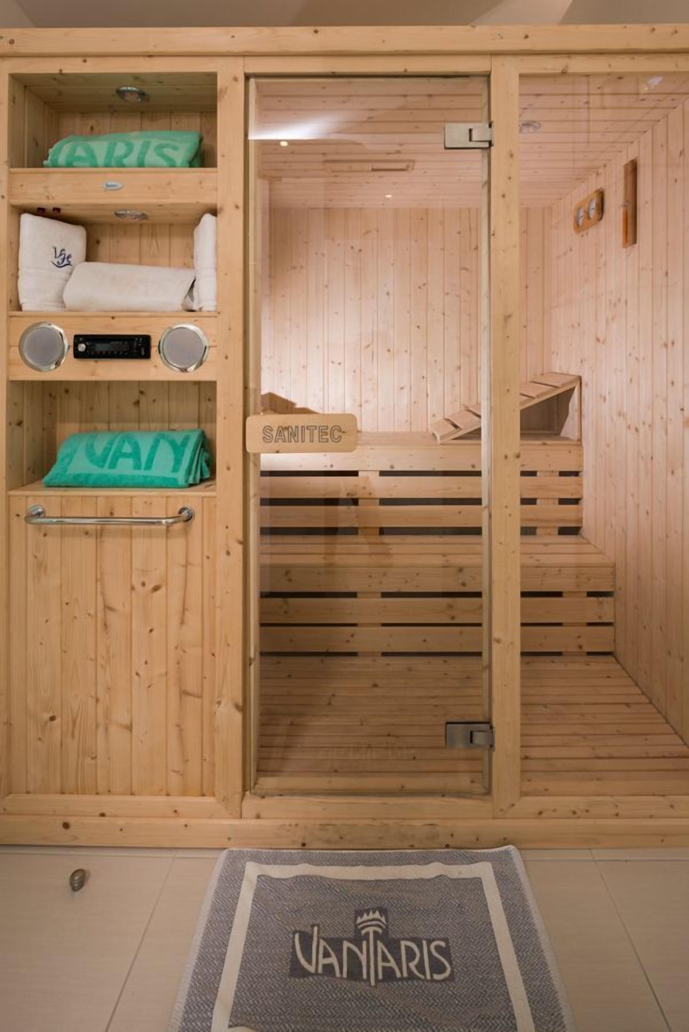 A wooden sauna with a bench, a towel rack, and a sign that reads "SANITEC".