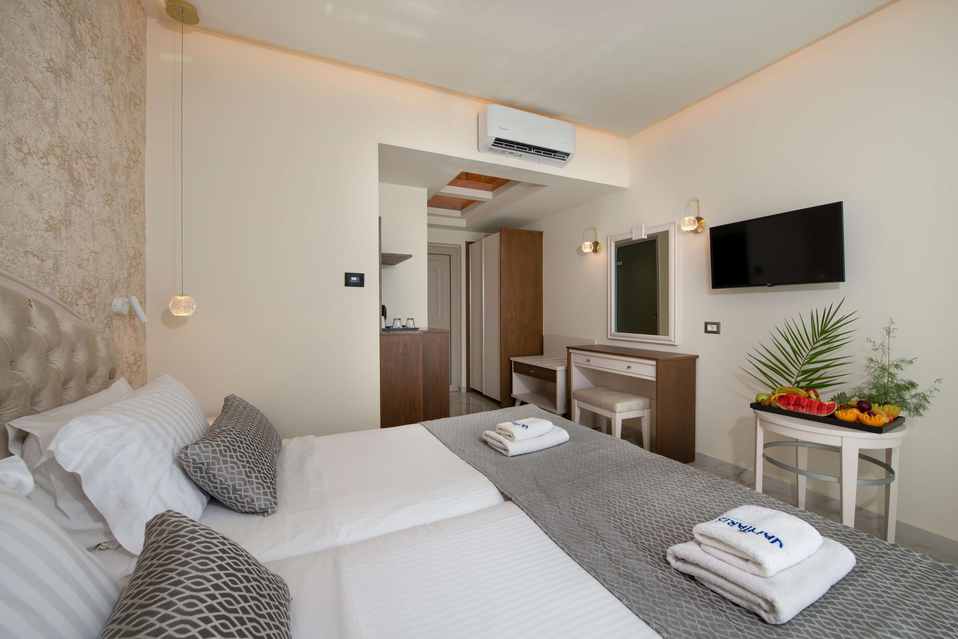 A modern hotel room with a large bed, a desk, a flat-screen TV, and a small table with fruit.