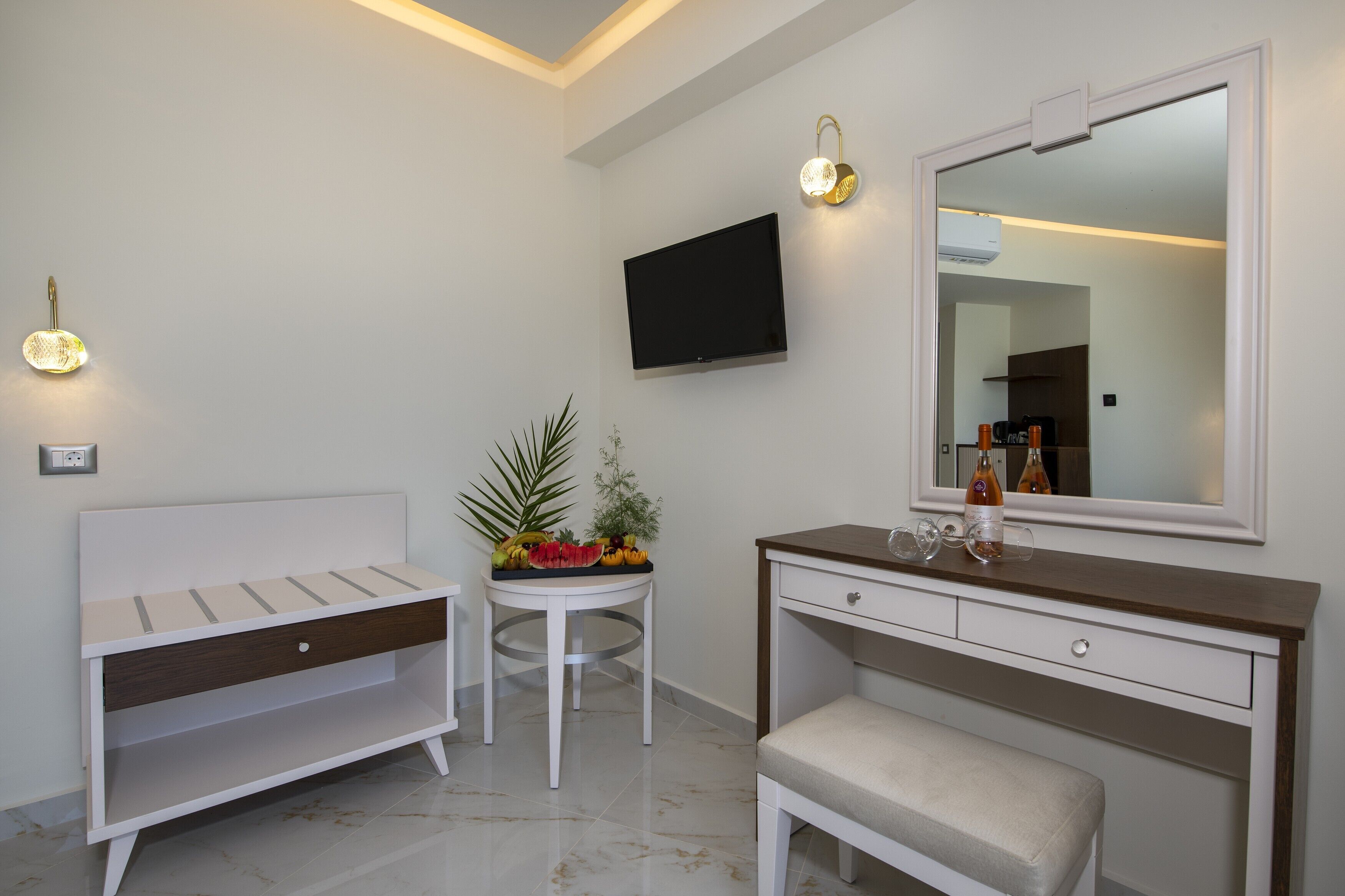 Une salle de bain moderne avec un meuble-lavabo blanc, un miroir, un téléviseur à écran plat et une petite table sur laquelle sont disposés des fruits.