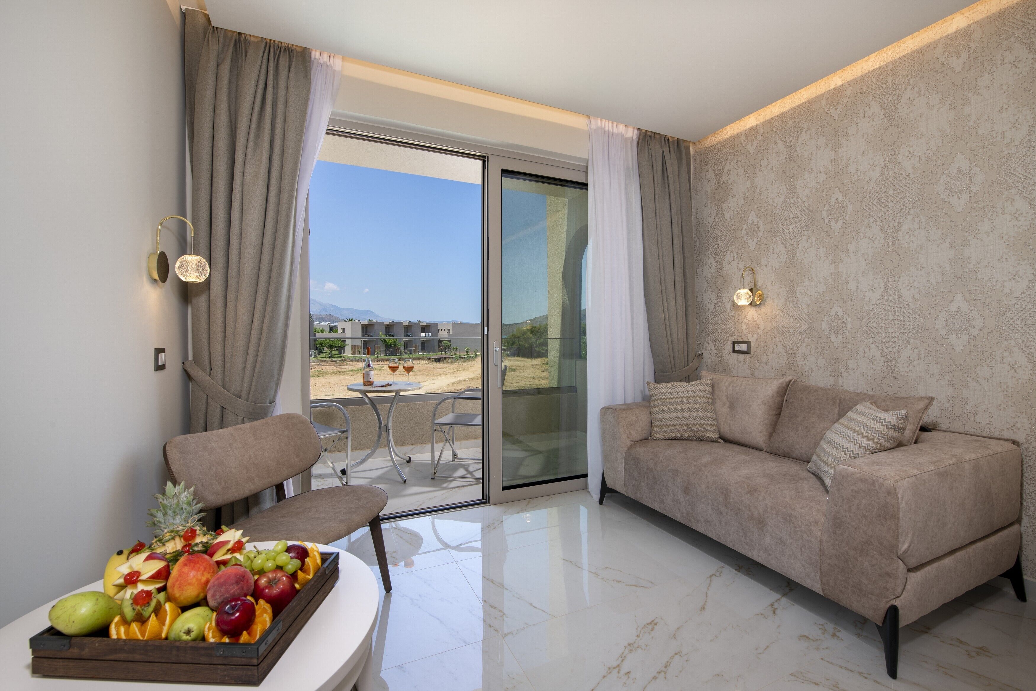 Una sala de estar moderna con un sofá, una mesa de comedor con fruta y un balcón con vistas a edificios y una montaña.