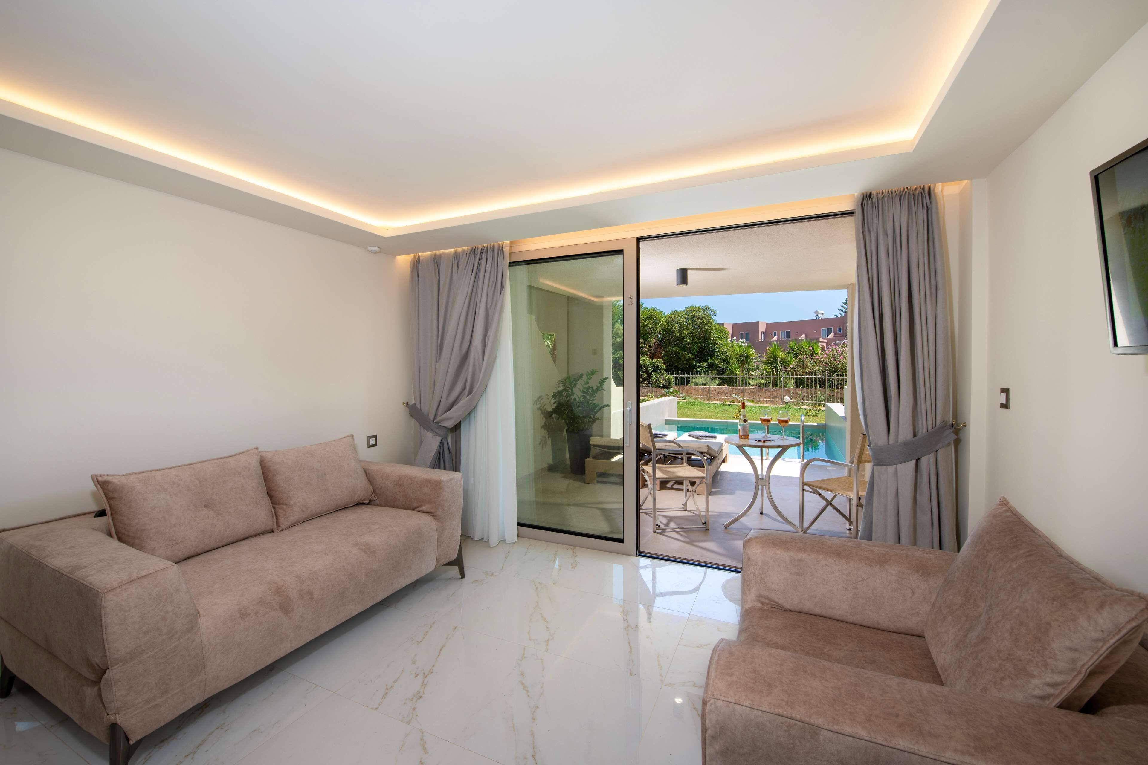 A modern living room with a sofa and armchairs, a glass door leading to a pool area, and a ceiling with recessed lighting.