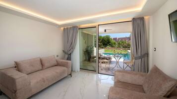 A modern living room with a sofa and armchairs, a glass door leading to a pool area, and a ceiling with recessed lighting.