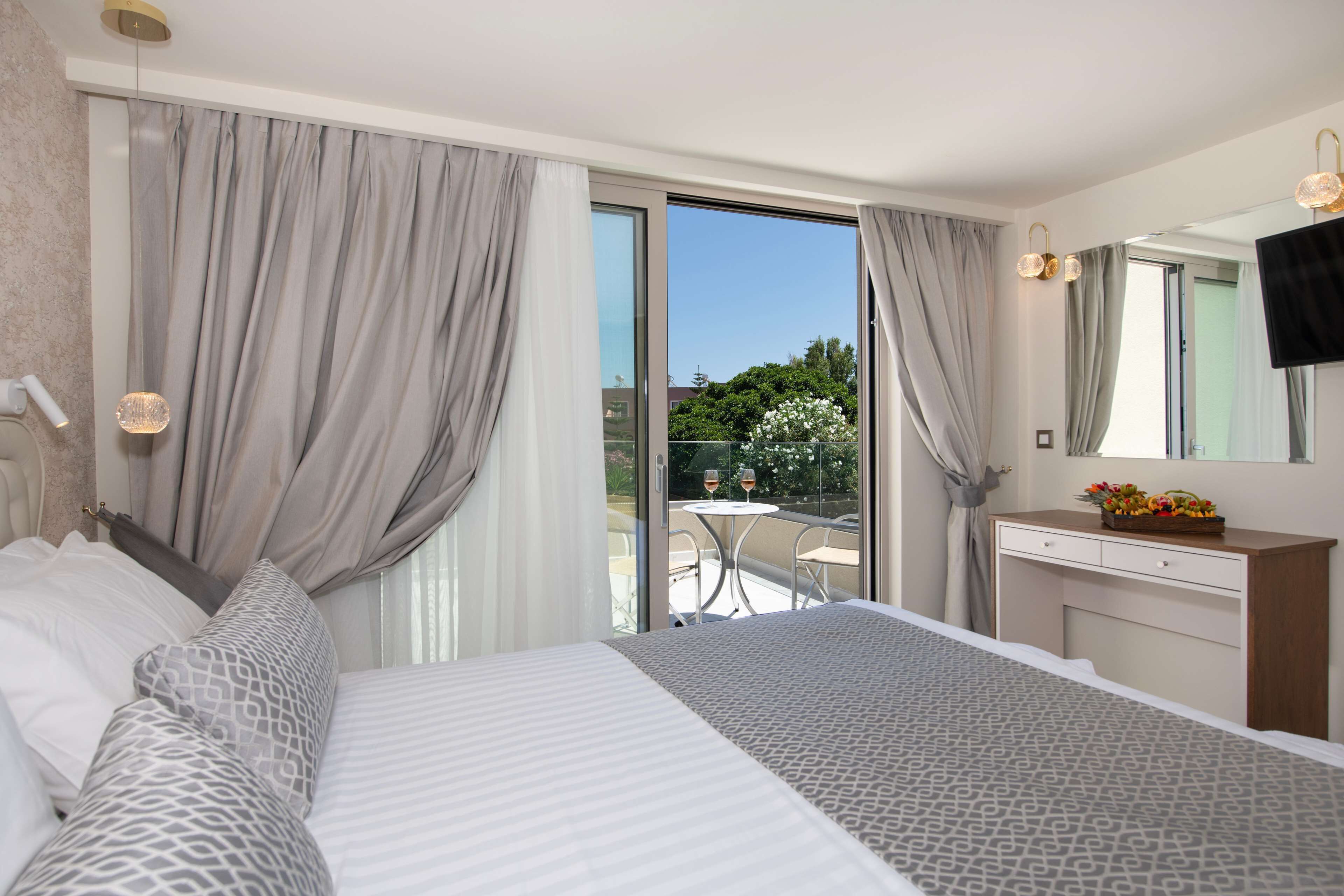 A hotel room with a large bed, a desk with a mirror, and a balcony with a table and chairs.