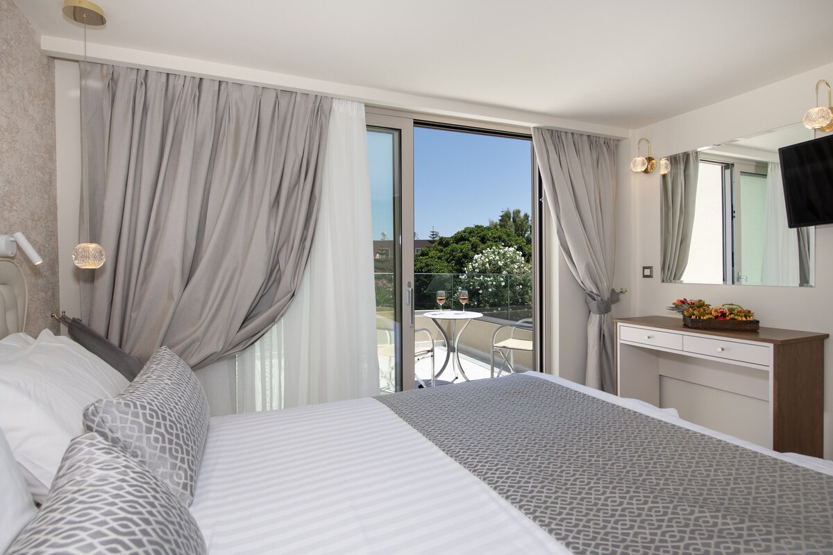 Habitación de hotel con cama, escritorio, silla y balcón con mesa y sillas.