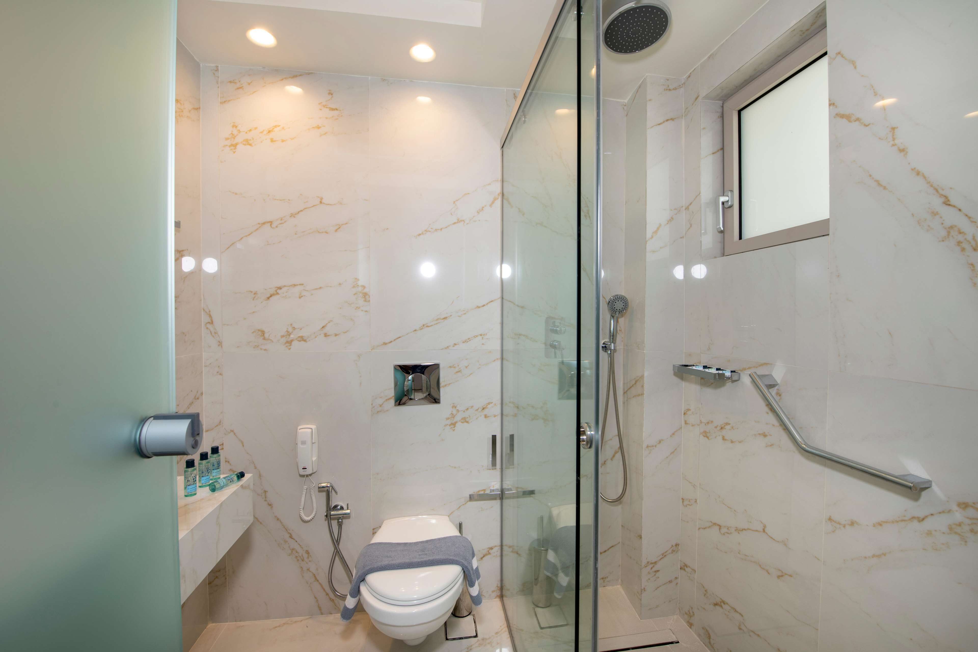 A modern bathroom with a glass-enclosed shower, a toilet, and a marble wall.
