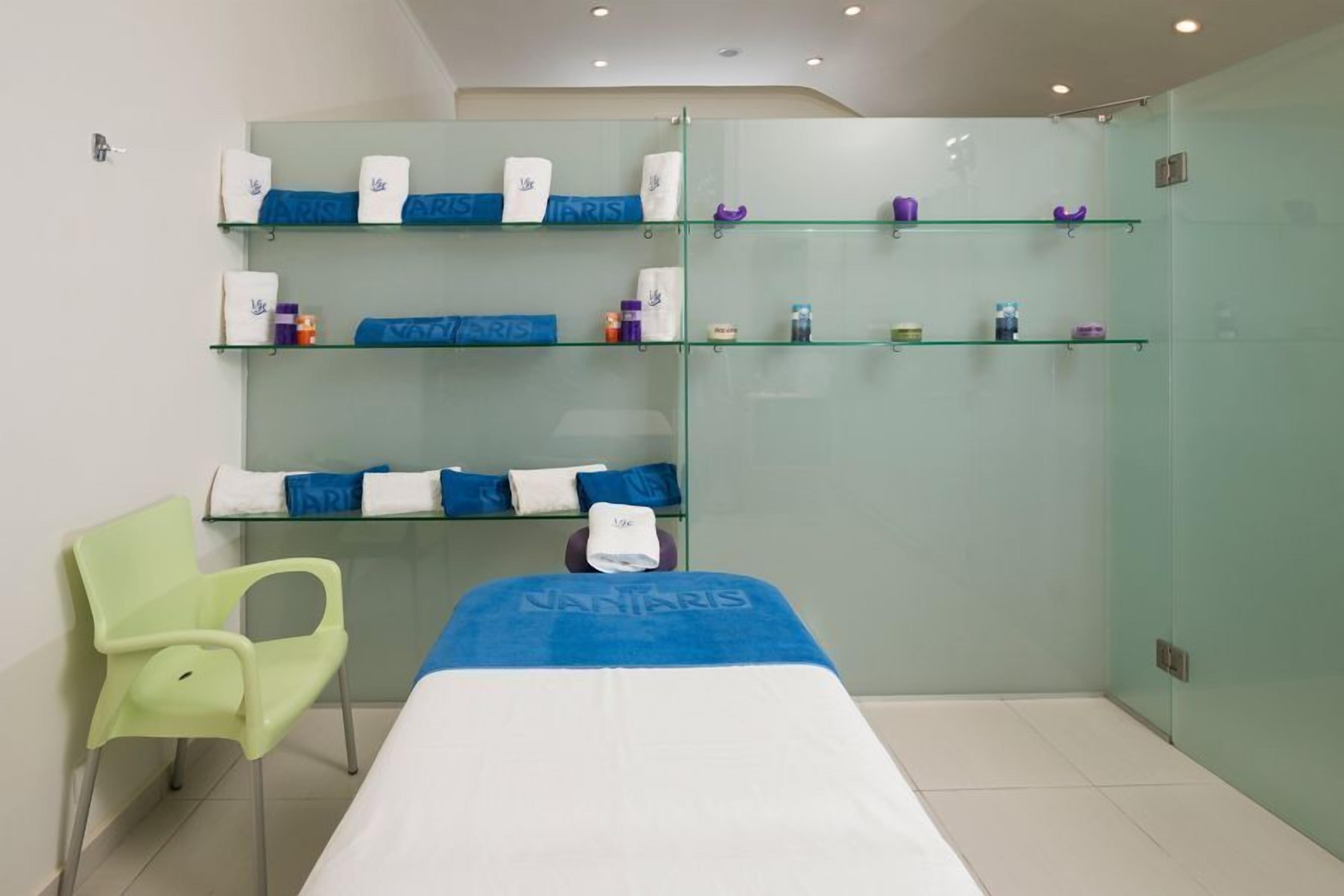 A modern bathroom with glass shelves, a green chair, and a bed with a towel.