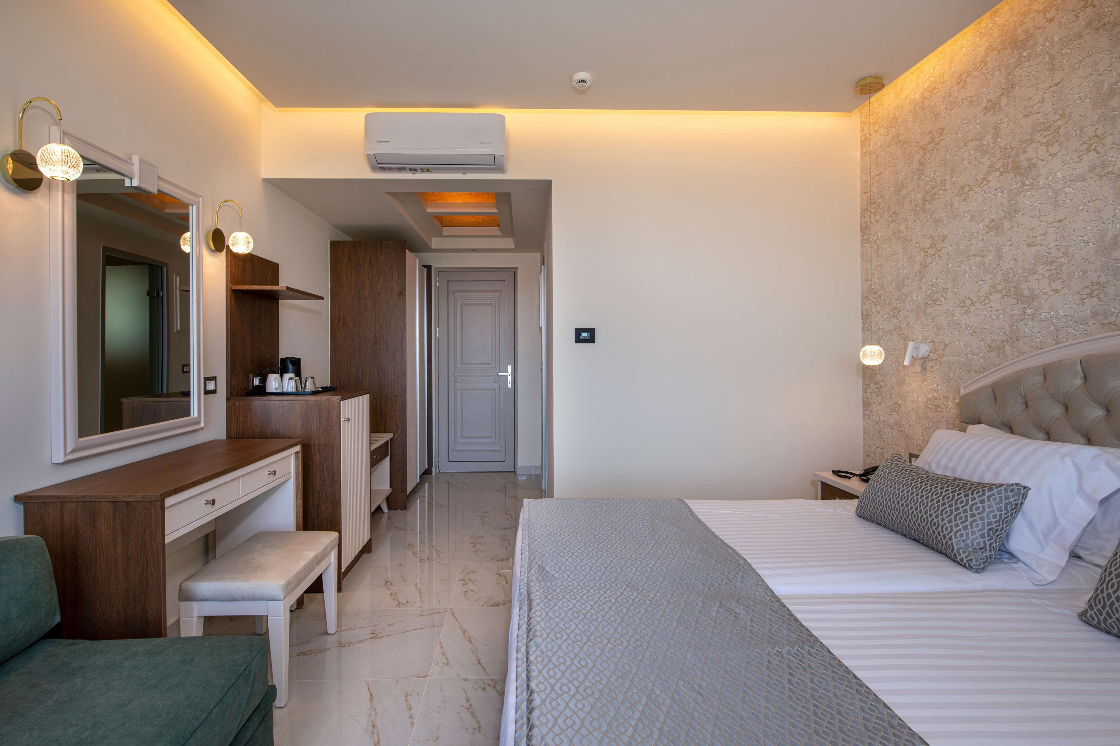 A modern bedroom with a bed, bedside table, nightstand, and a dresser. There is a mirror, a bench, and a door leading to another room.