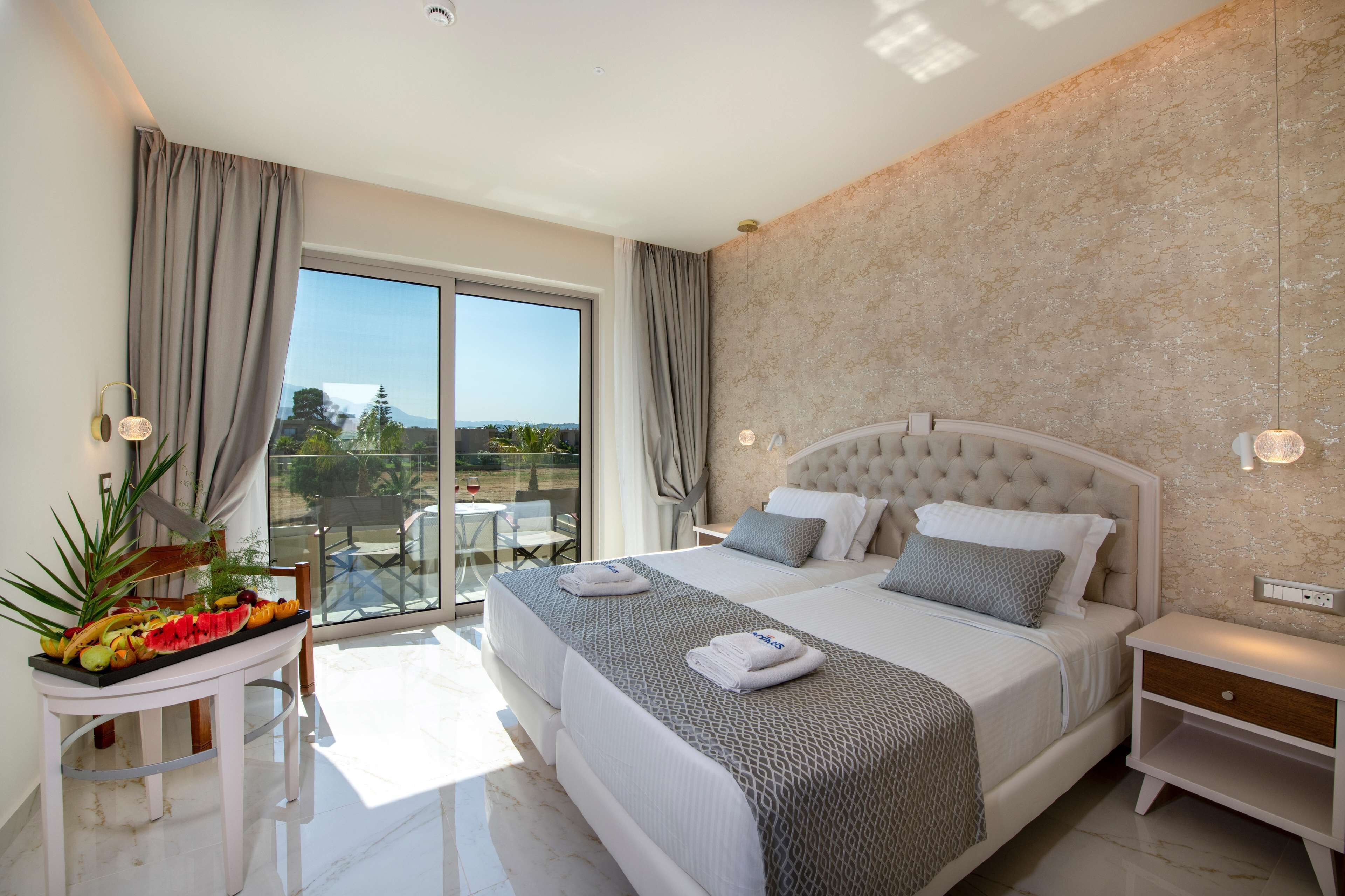 A bedroom with a large bed, a bedside table, a nightstand, a window with curtains, and a view of the outdoors.