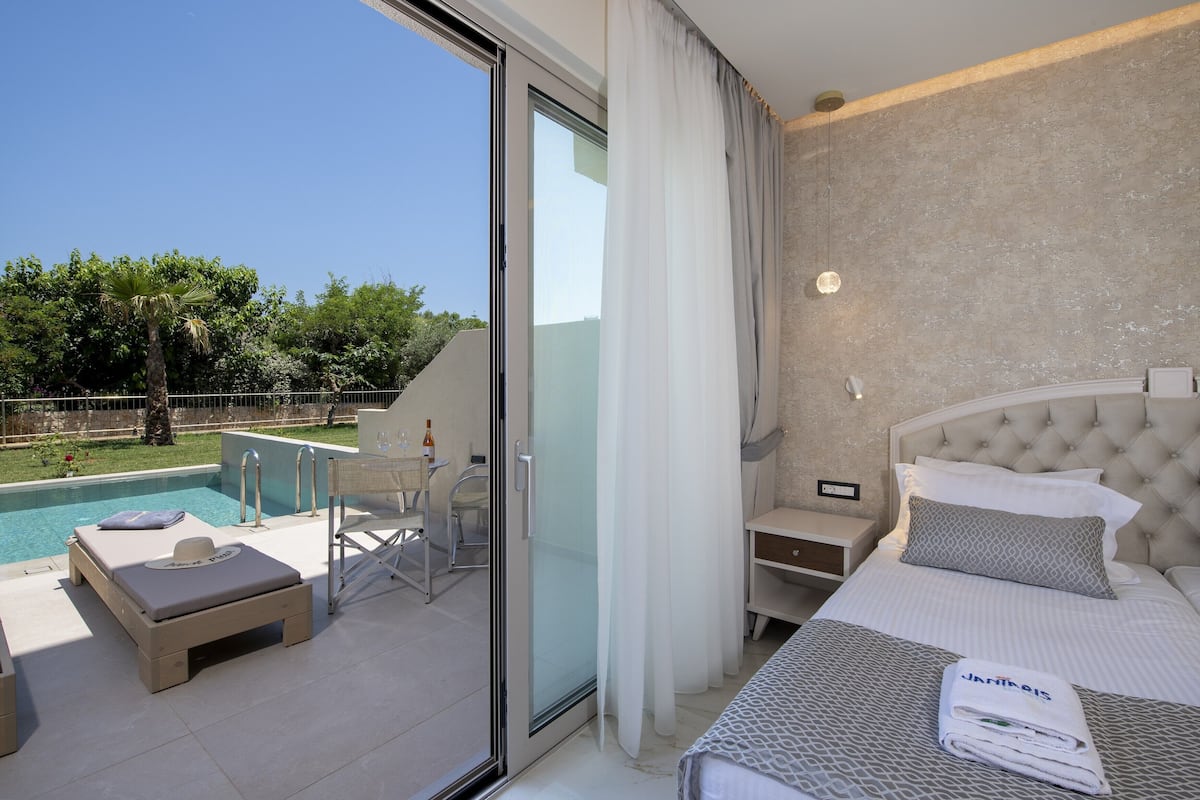 Quarto de hotel com cama, pequena mesa de trabalho, cadeira, piscina e vista para o exterior.