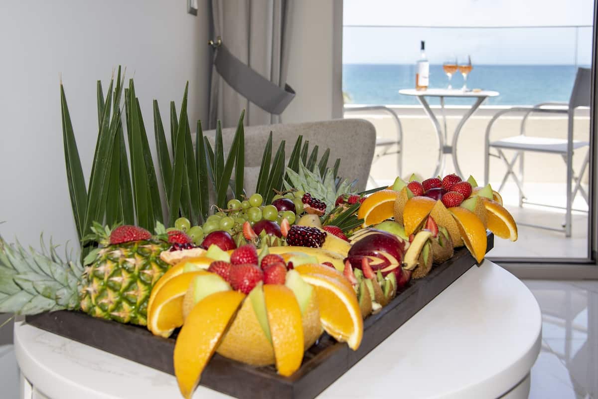 Uma travessa de frutas sobre uma mesa, com vista para a praia e para o oceano ao fundo.