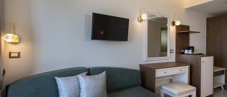 A modern hotel room with a green sofa, a small bedside table, a mirror, a flat-screen TV, and a built-in wardrobe.
