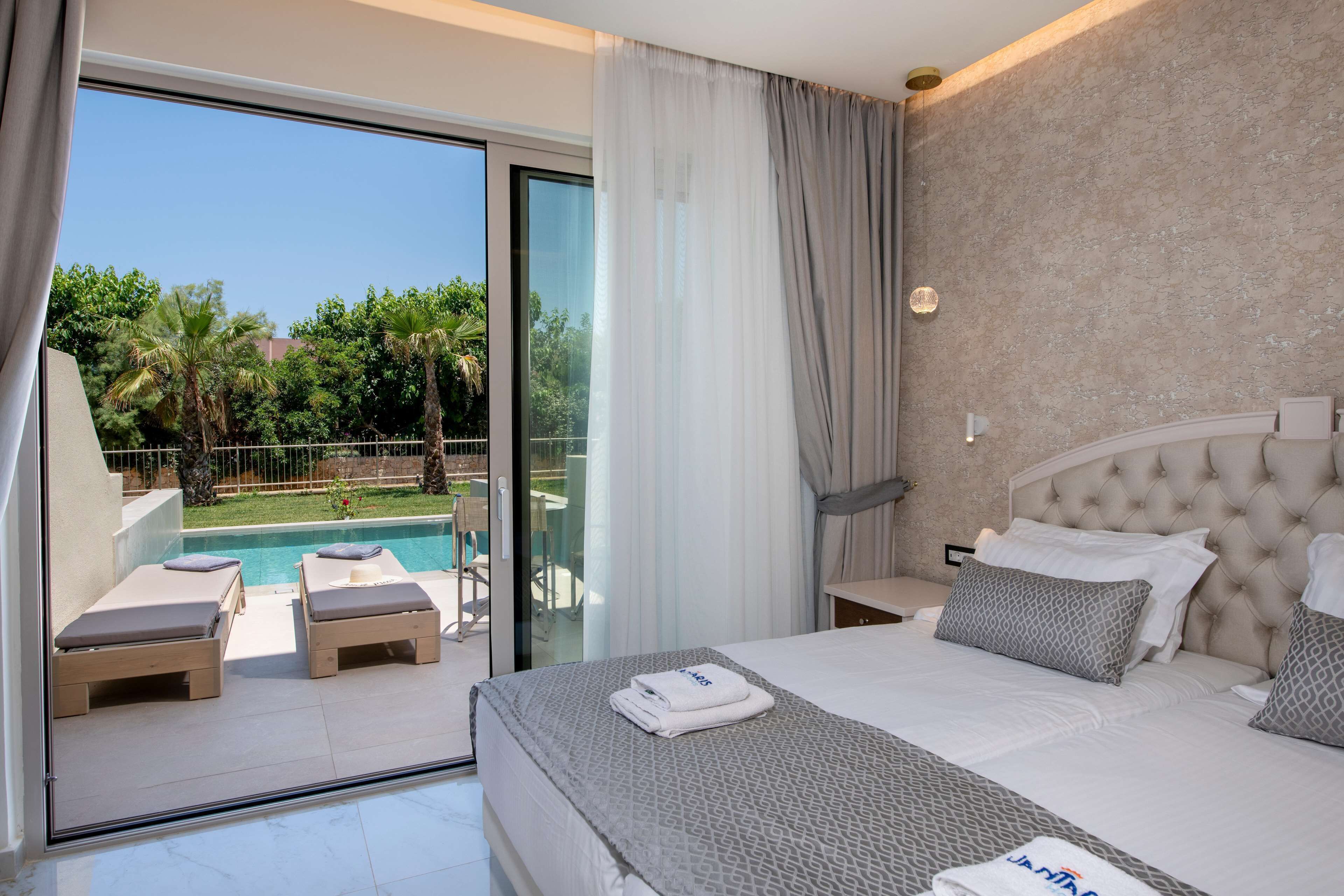 Quarto de hotel com cama, vista para uma piscina e varanda com cadeiras de descanso.