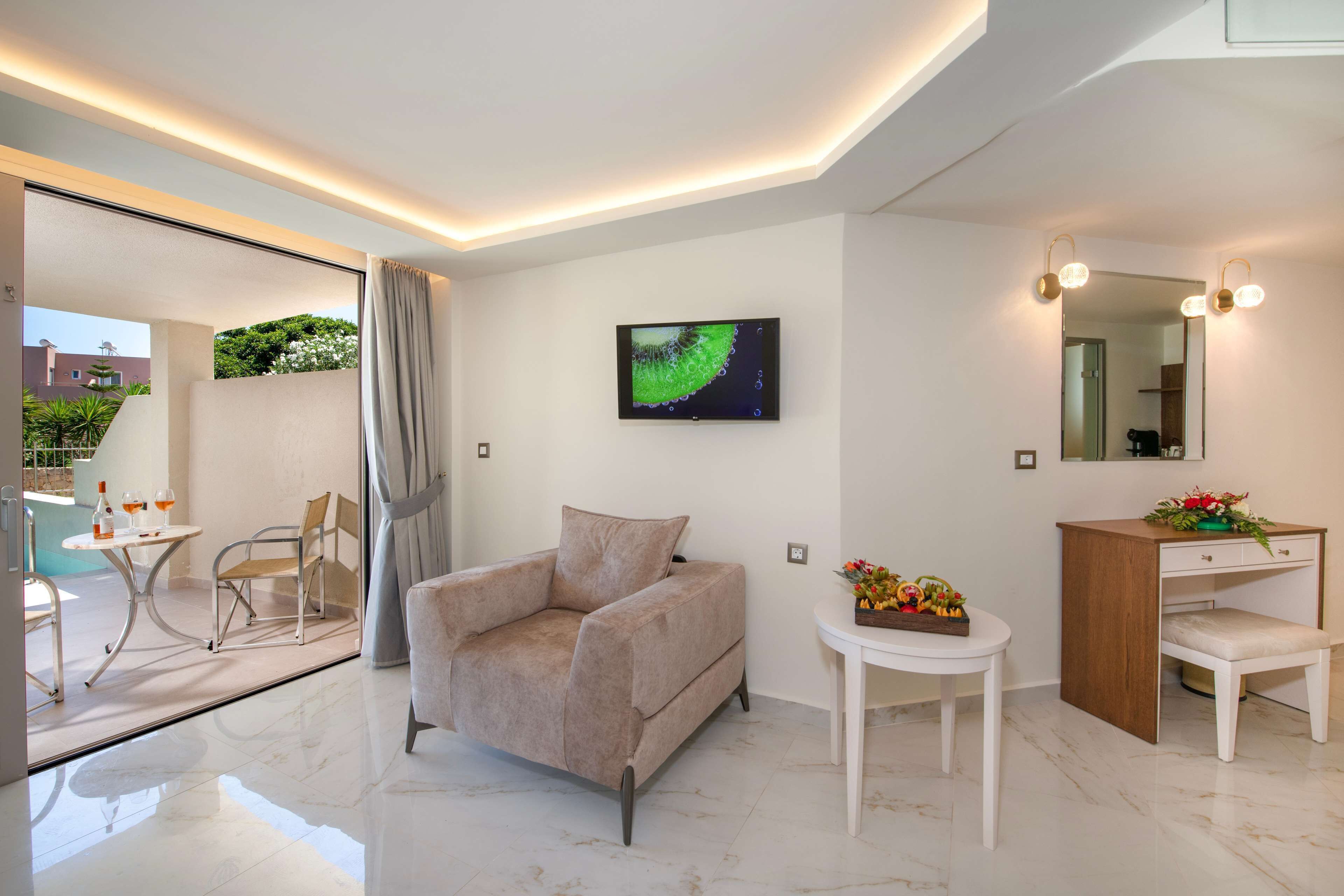 Una habitación de hotel moderna con un sofá, una mesita con un florero, una tocador con espejo y un televisor montado en la pared.