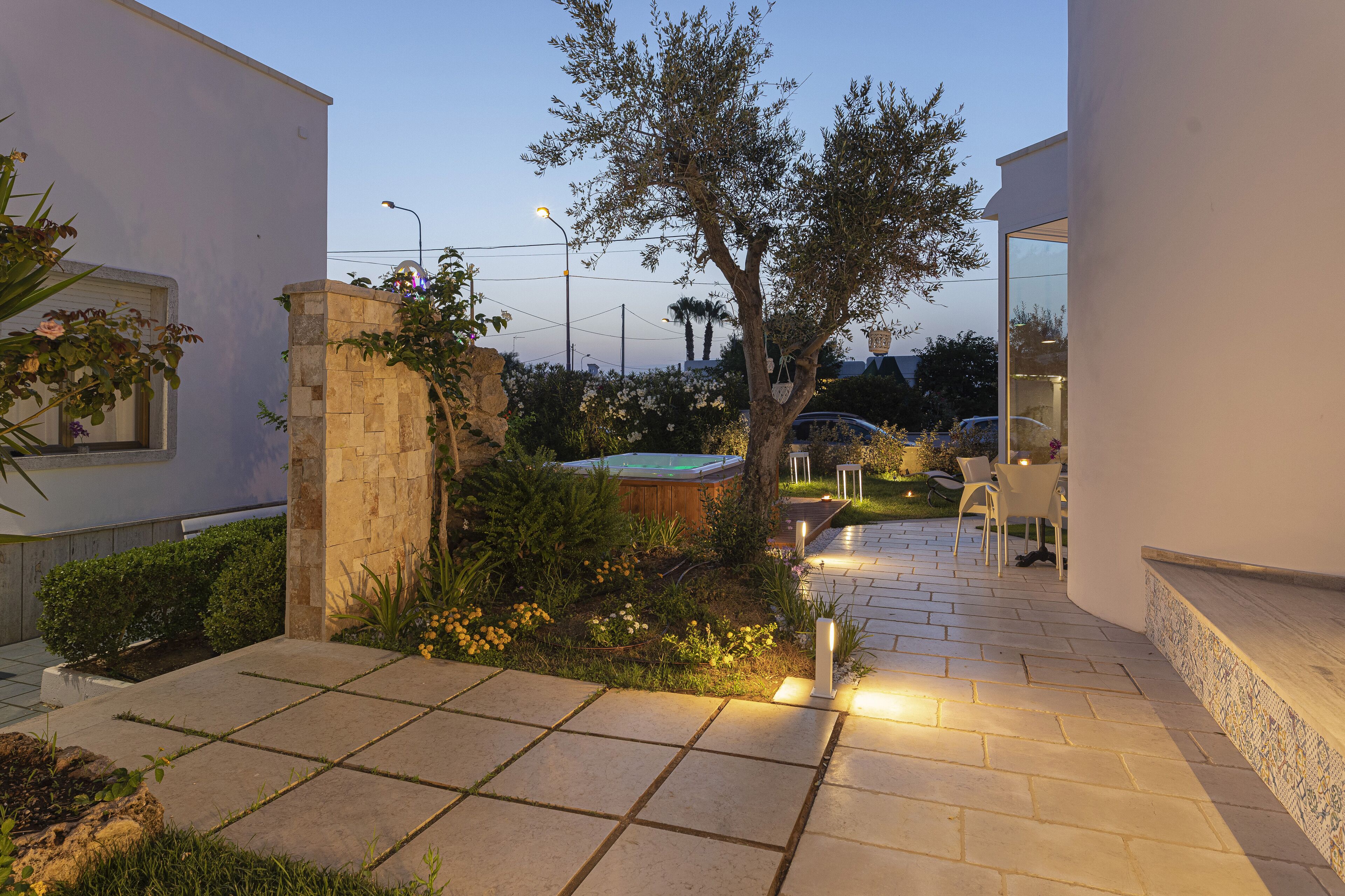 A modern outdoor patio with a stone pathway, a wooden hot tub, and white chairs.
