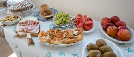 Uma mesa com diversos alimentos, incluindo pizza, frutas e bolo.