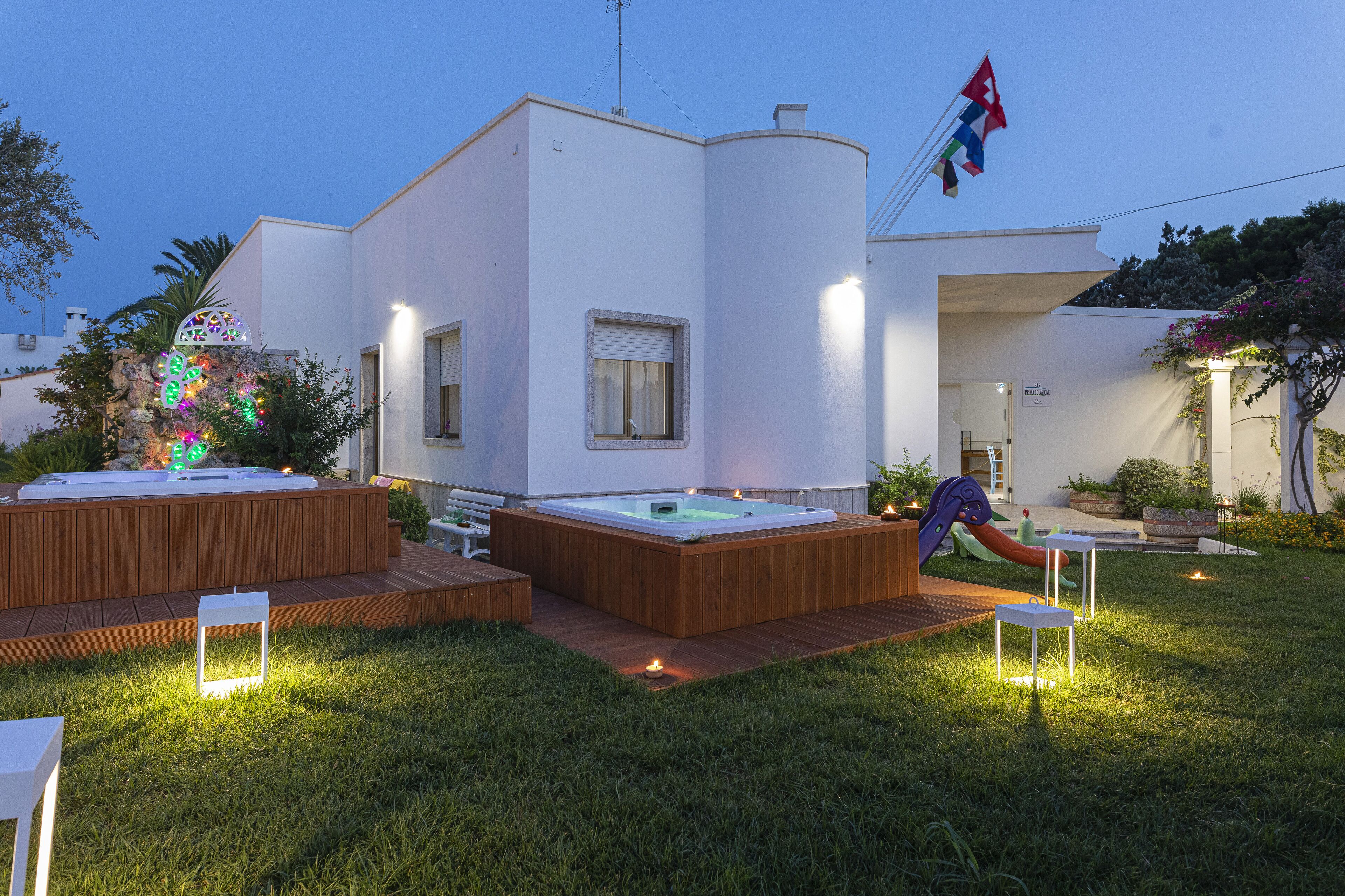 A modern outdoor pool area with a hot tub, wooden deck, and a flag.