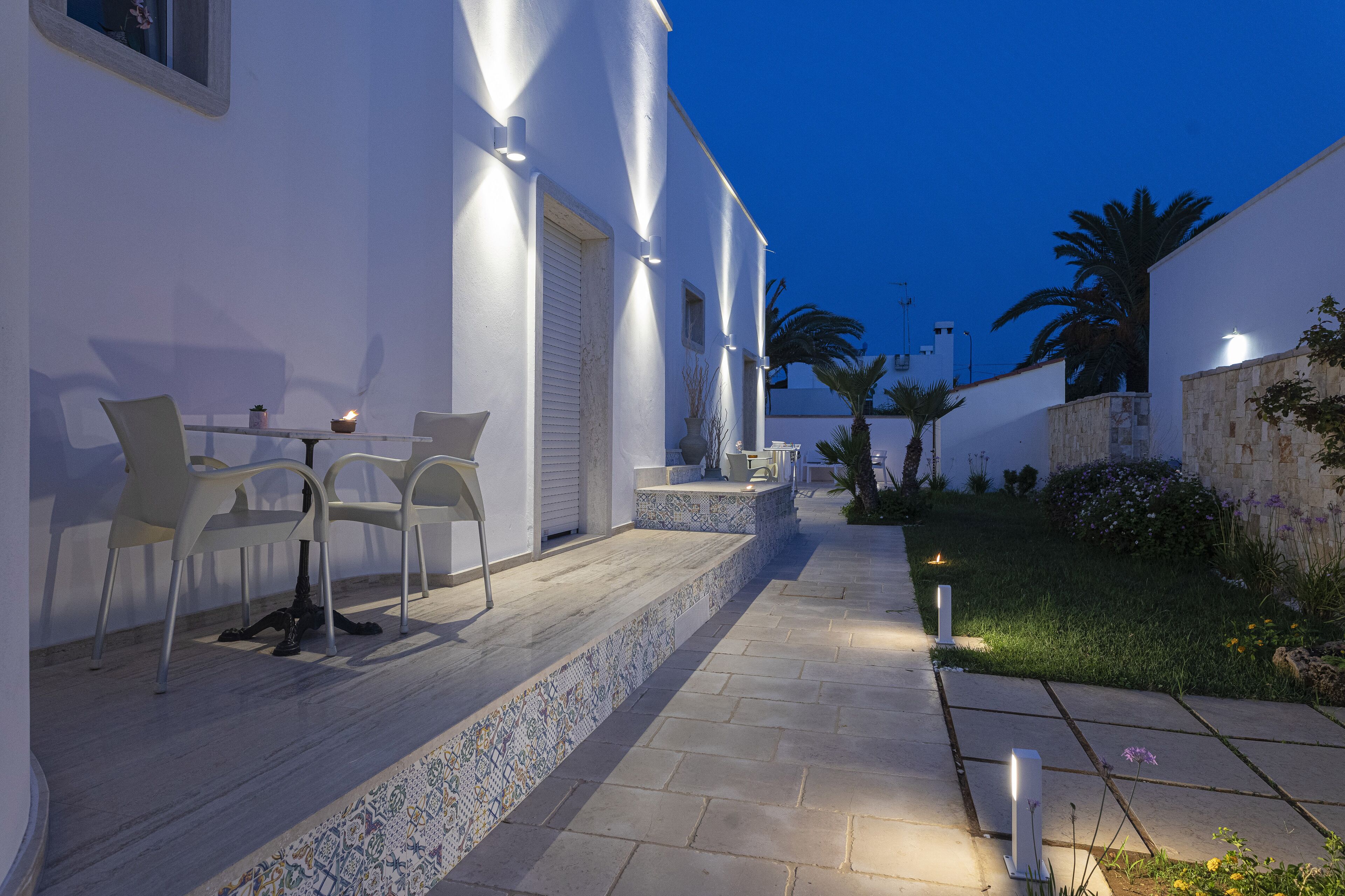 A modern outdoor patio with white walls, a tiled floor, and a few chairs.