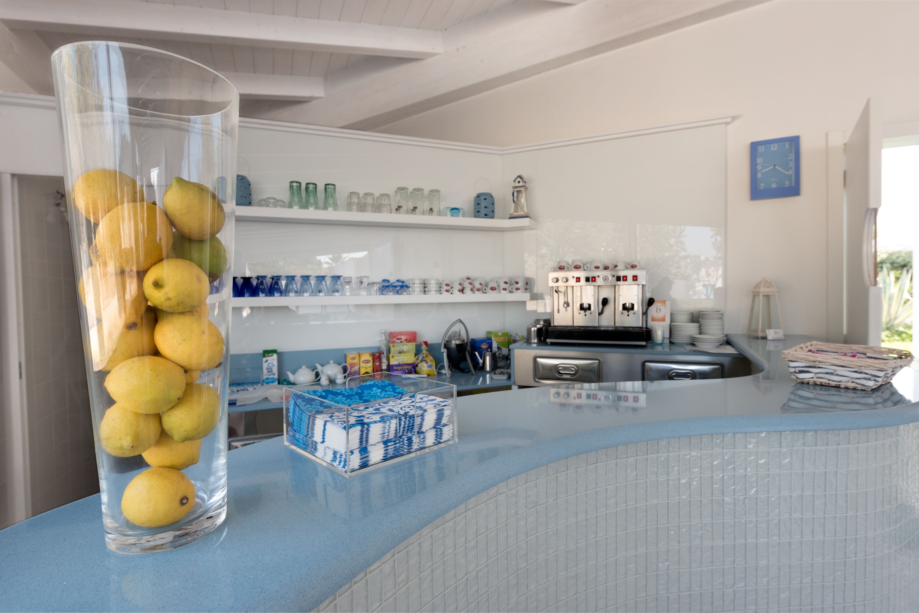 Une cuisine avec un vase en verre transparent rempli de citrons, un mur recouvert de carreaux bleus et divers appareils de cuisine.