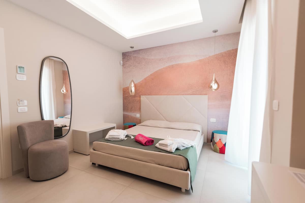 Un dormitorio moderno con una cama, una silla, una mesita de noche, un espejo y una pared con diseño texturizado.