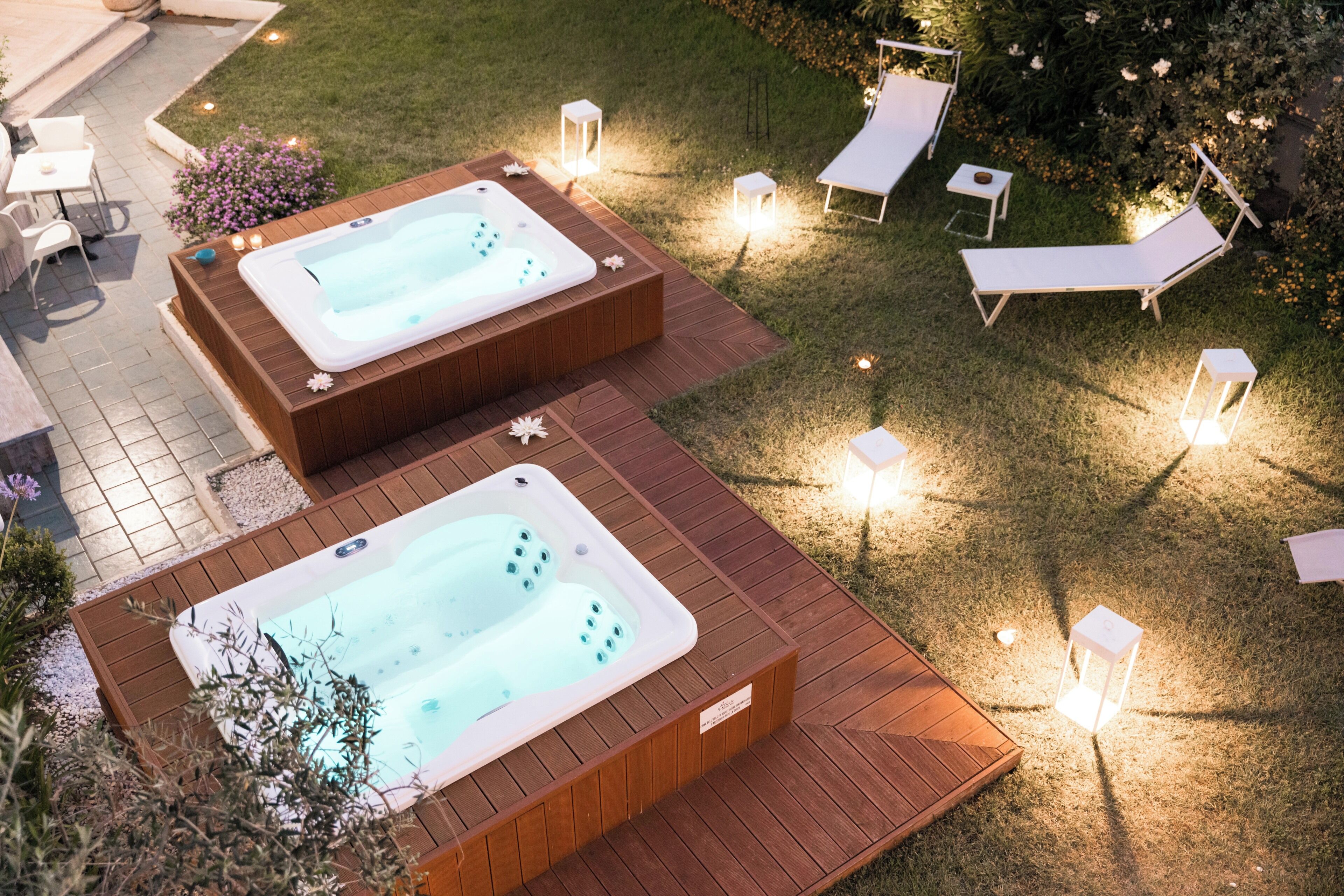 Zwei Whirlpools auf einer Holzterrasse mit Liegestühlen und Kerzen.
