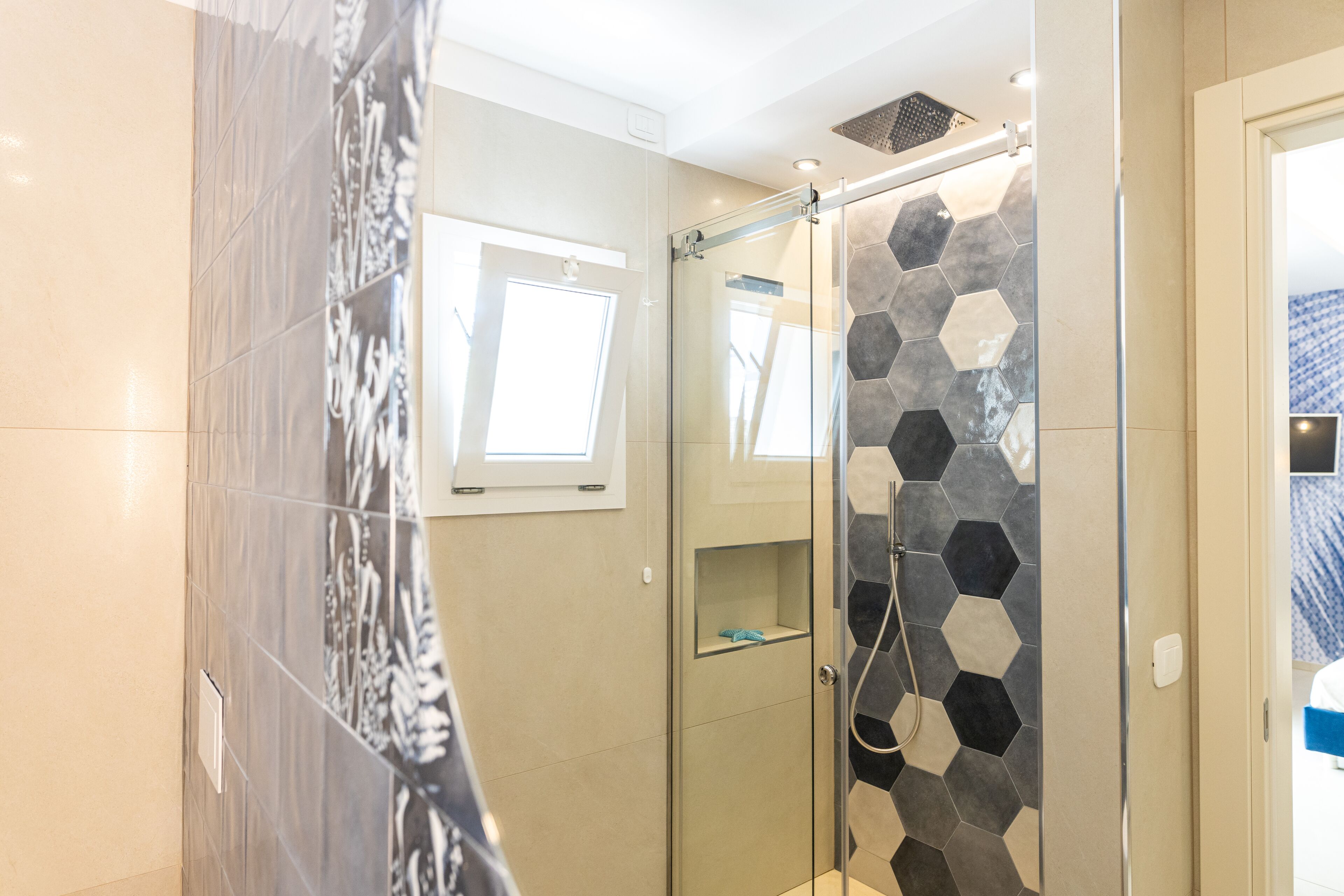 A modern bathroom with a glass shower enclosure, a small window, and a hexagonal tile backsplash.