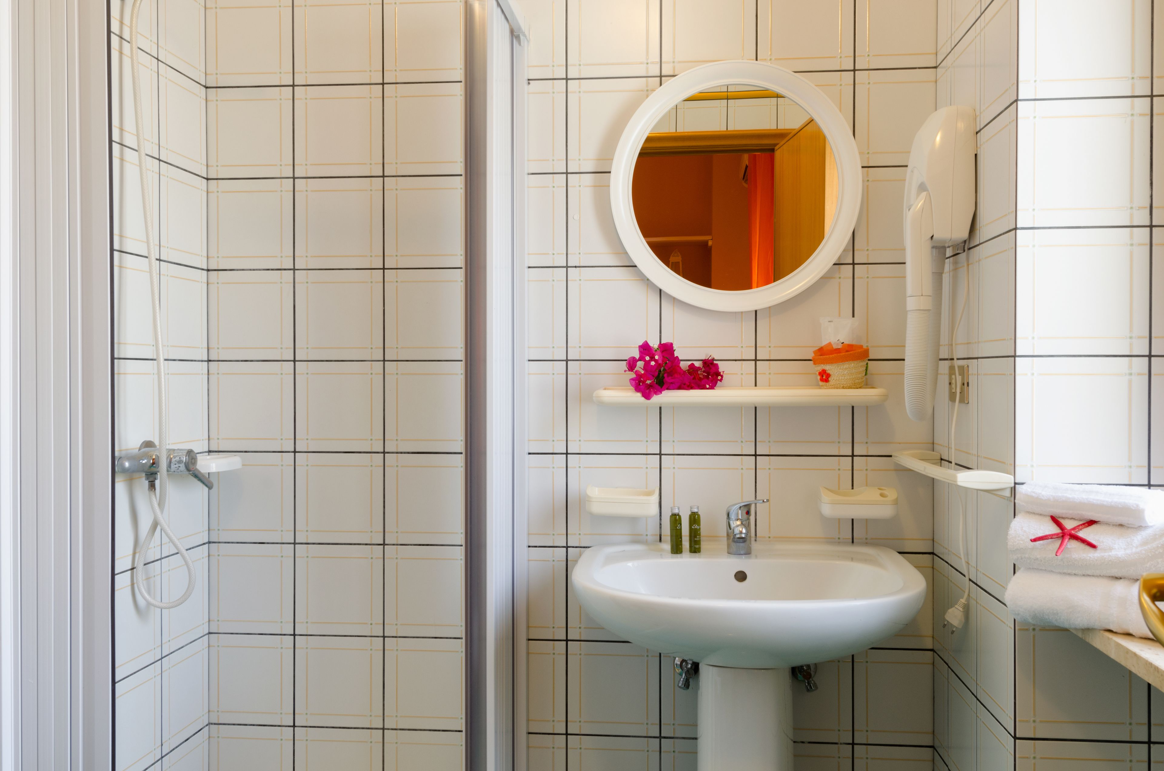 A bathroom with a white sink, a mirror, a shower, and a toilet.