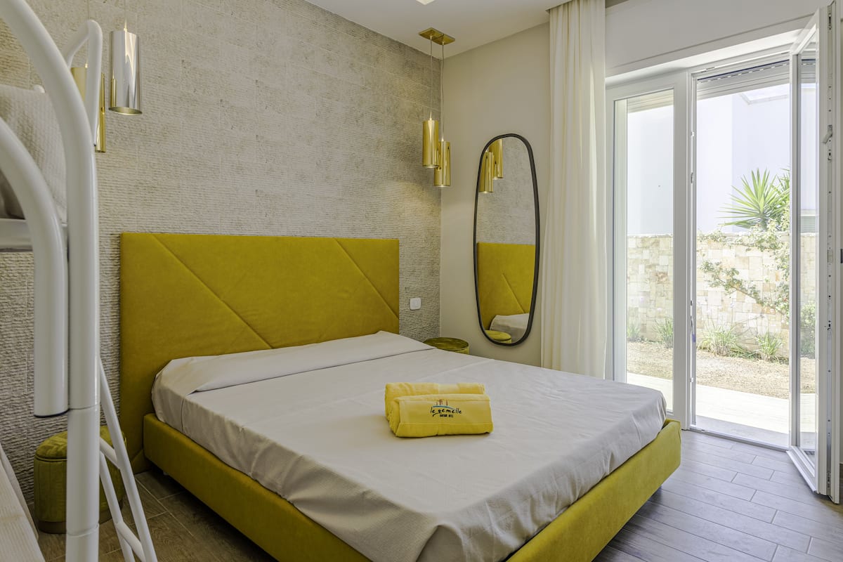 Habitación de hotel con cama, cabecera amarilla, un espejo grande y vistas al exterior.