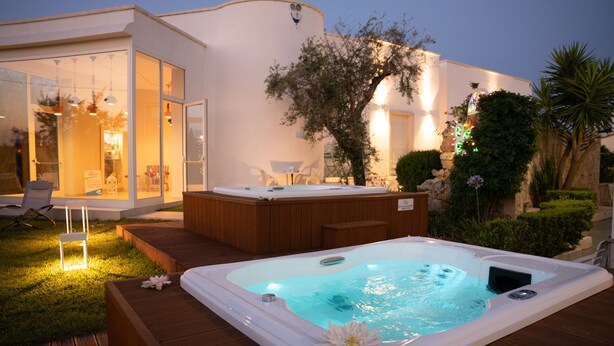 Een hottub op een houten terras, met een glazen ruimte op de achtergrond.