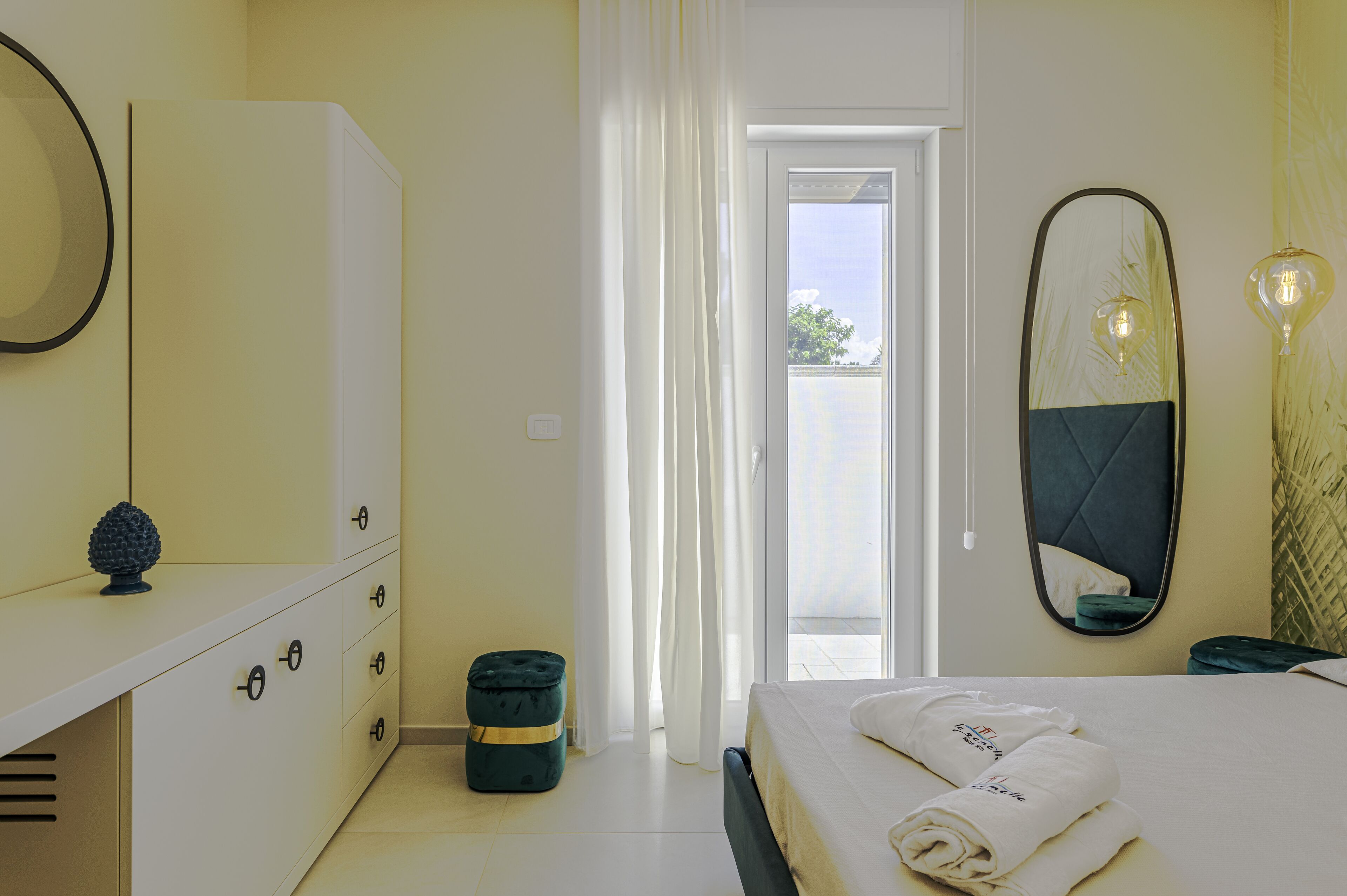 Una habitación de hotel con cama, armario, espejo y ventana con cortinas.