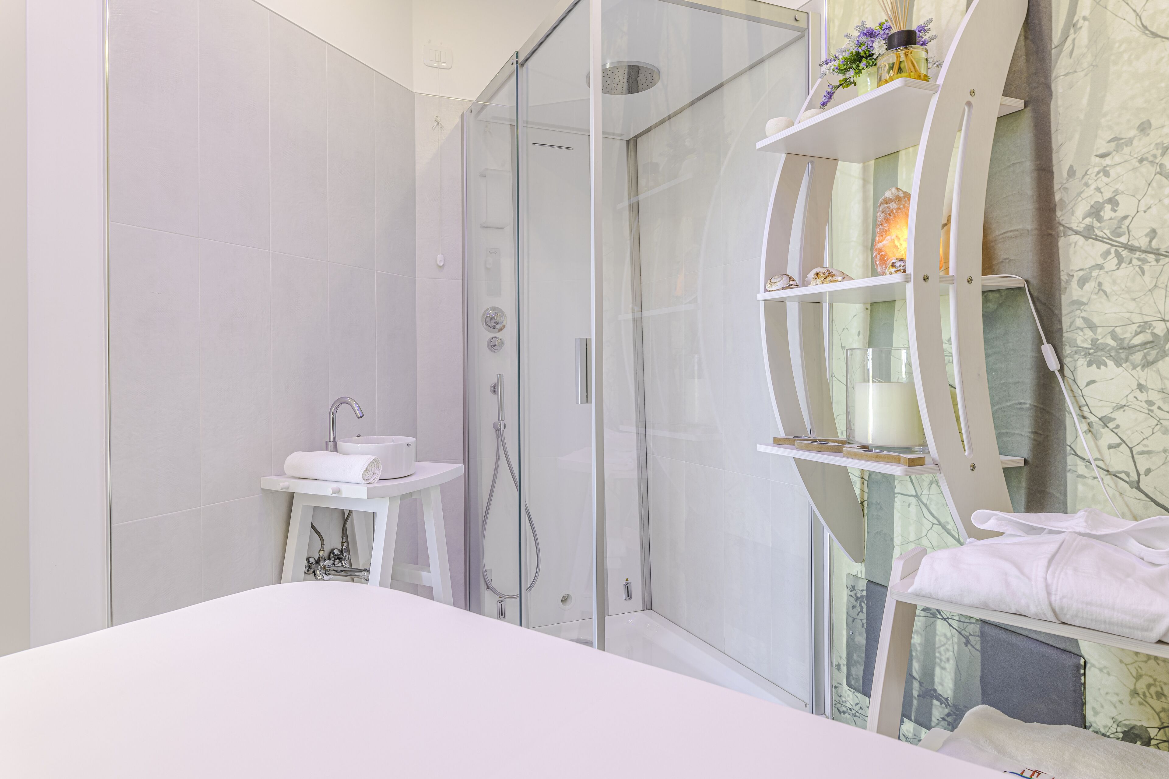 A modern bathroom with a glass-enclosed shower, a white sink, and a vanity with shelves.