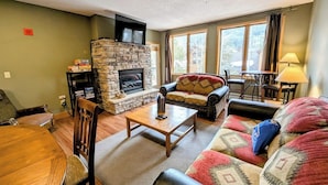 A cozy living room with a stone fireplace, a sofa, a coffee table, and a dining area. - Gateway Lodge 5030 by SummitCove Vacation Lodging (Keystone)